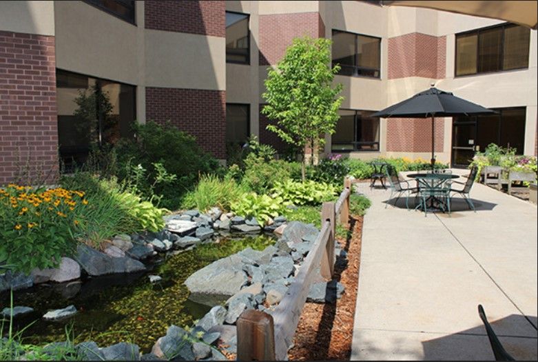 A serene courtyard with a pond, lush greenery, and outdoor seating surrounded by a building's exterior.