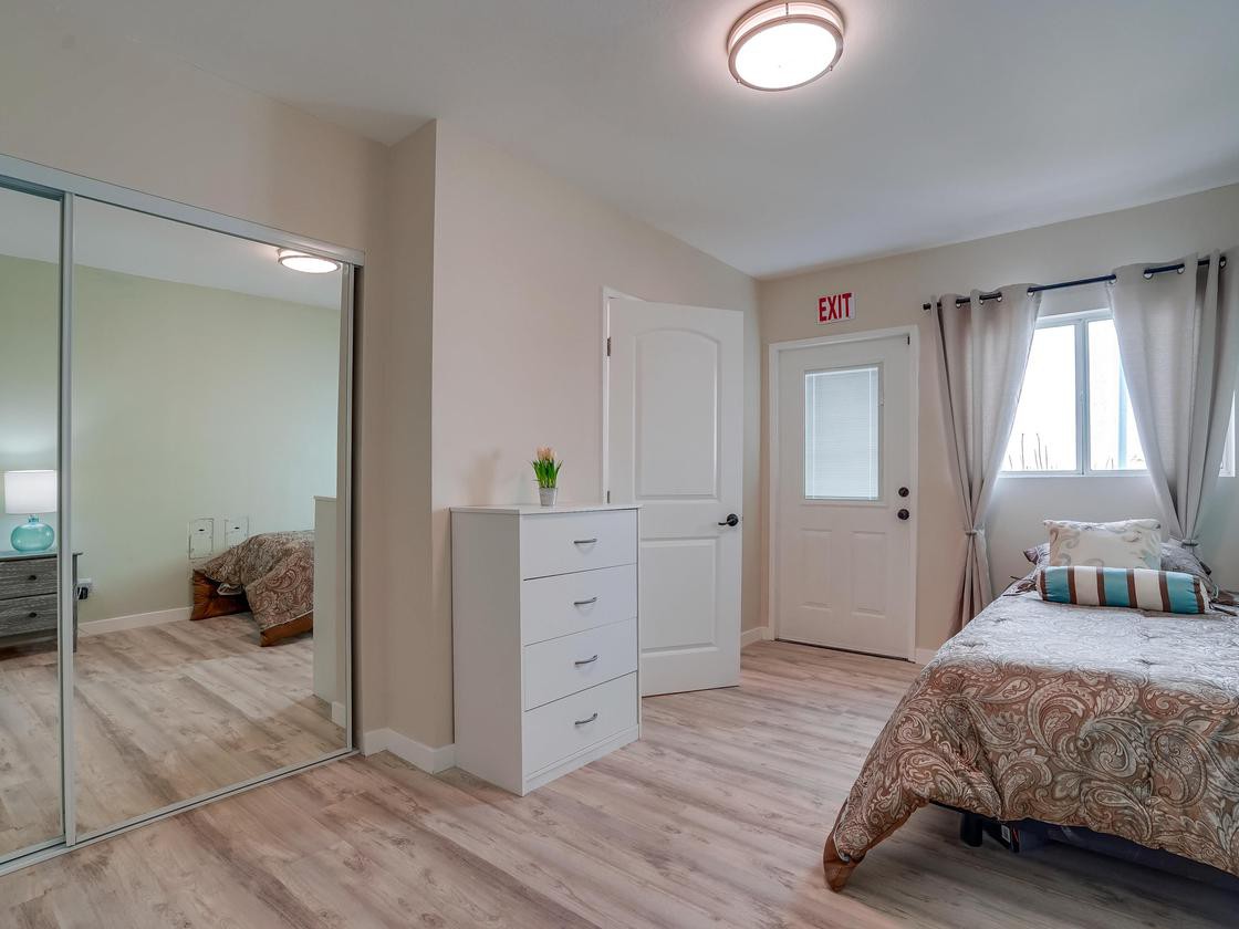 A tidy bedroom with a dresser and a bed, featuring light-colored flooring and curtains.
