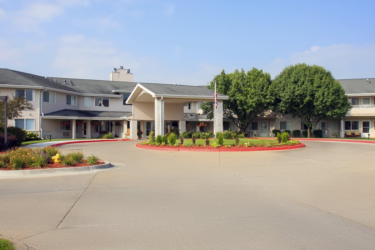 A two-story building with a circular driveway surrounded by neatly trimmed bushes and trees.