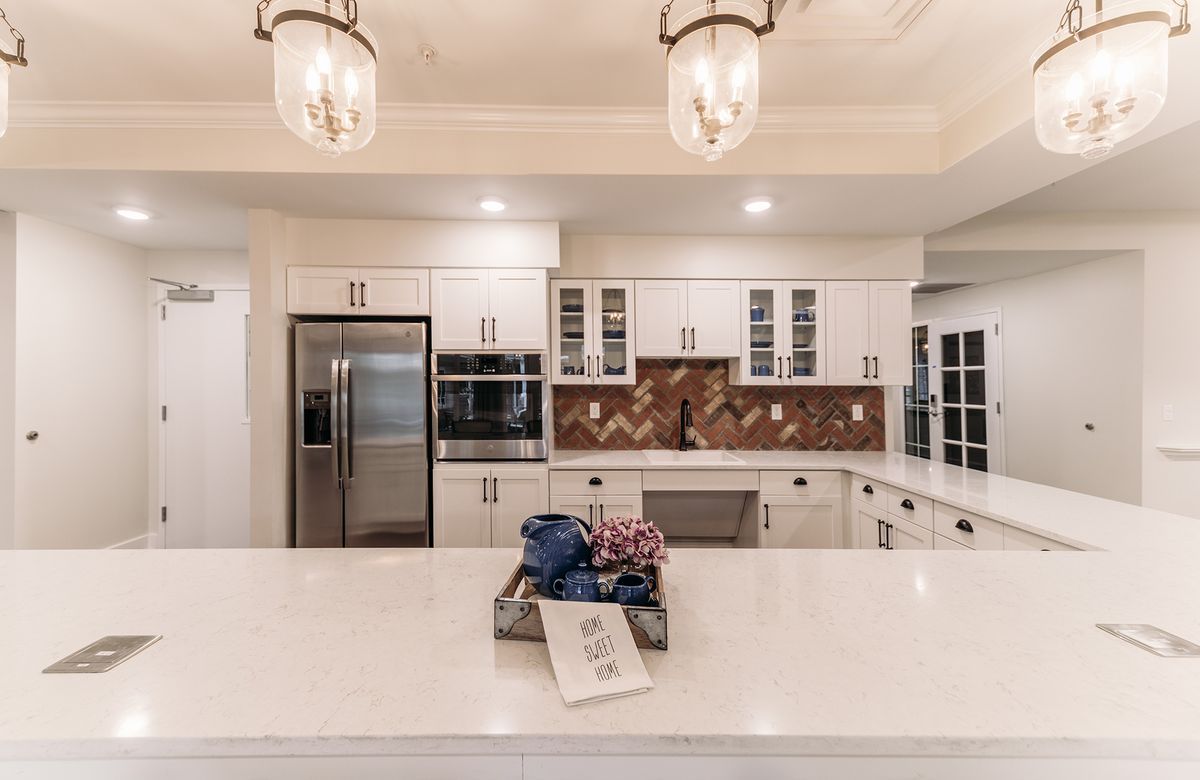 A modern kitchen with white cabinets, an island, and stainless steel appliances, highlighted by elegant pendant lights and a decorative backsplash.