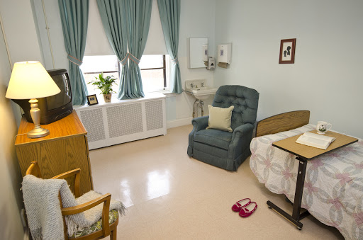 A cozy hospital room featuring a bed, comfortable chair, and a small TV.