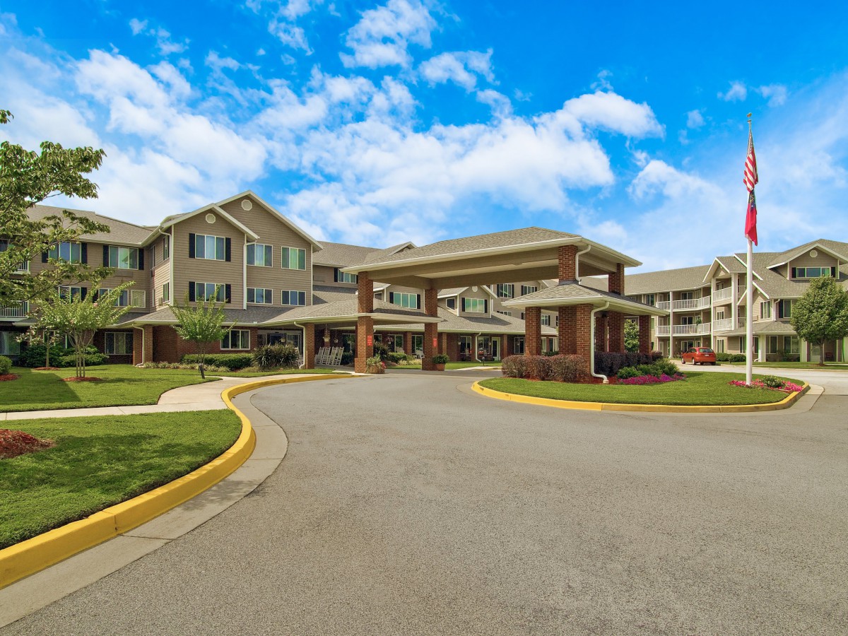 A view of a large residential building with a circular driveway and neatly maintained landscaping under a partially cloudy sky.