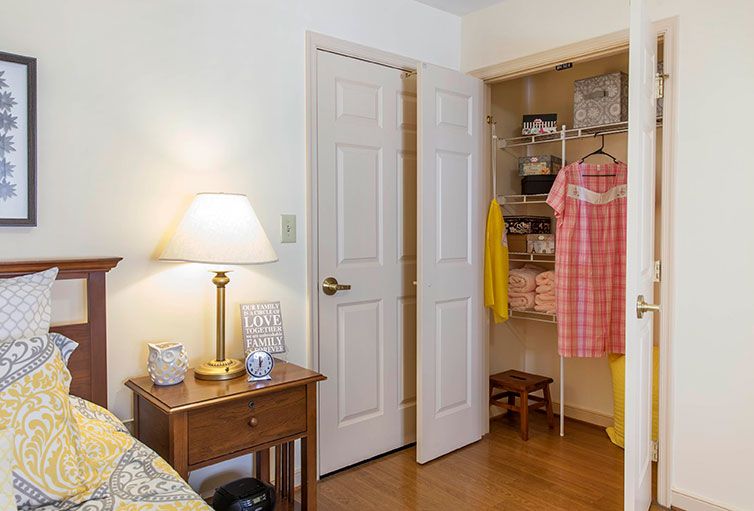 A cozy bedroom with an open closet displaying clothing, a lamp on the nightstand, and inviting decor.