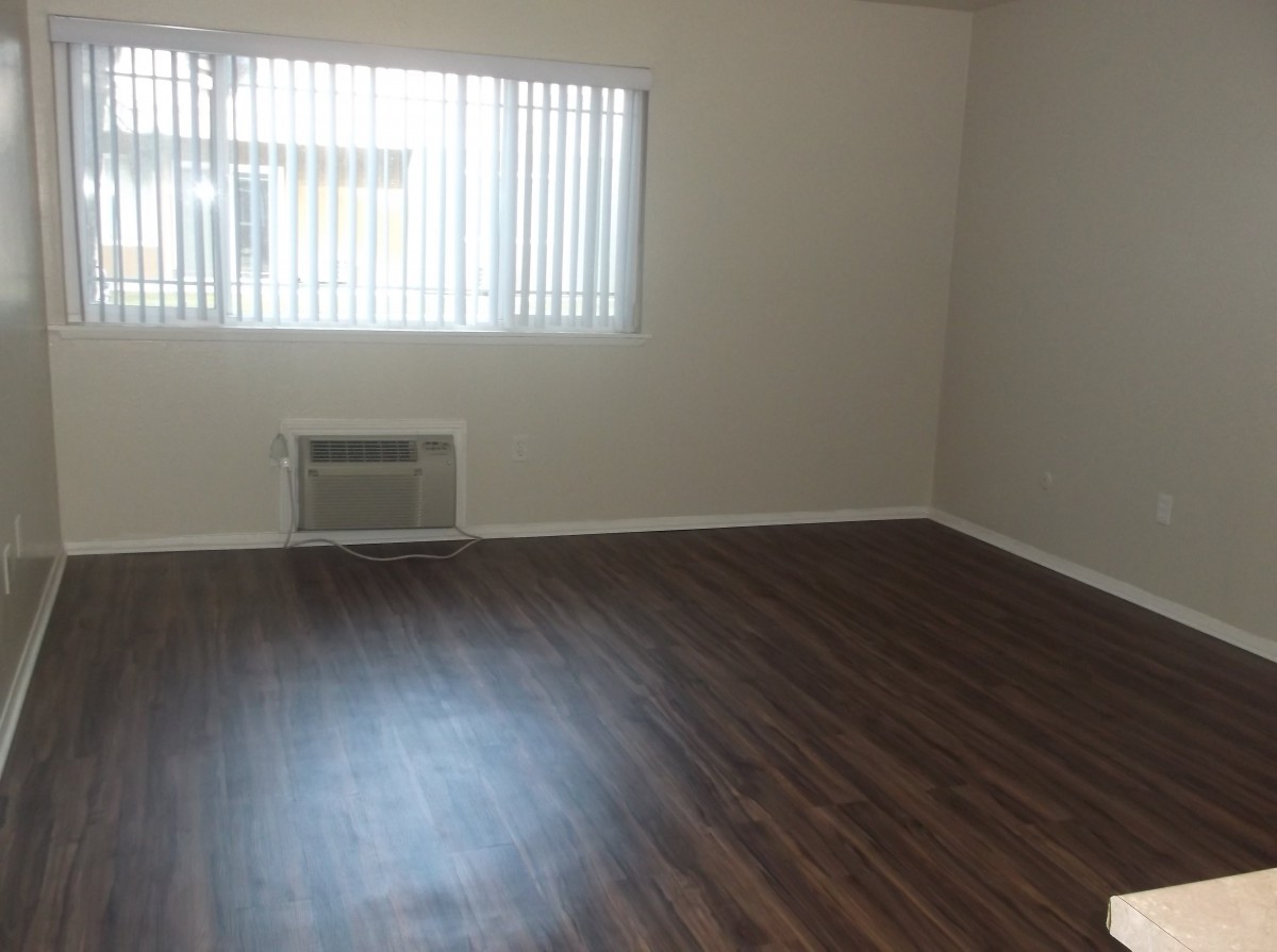 An empty room with hardwood flooring and a window with blinds, featuring an air conditioner.