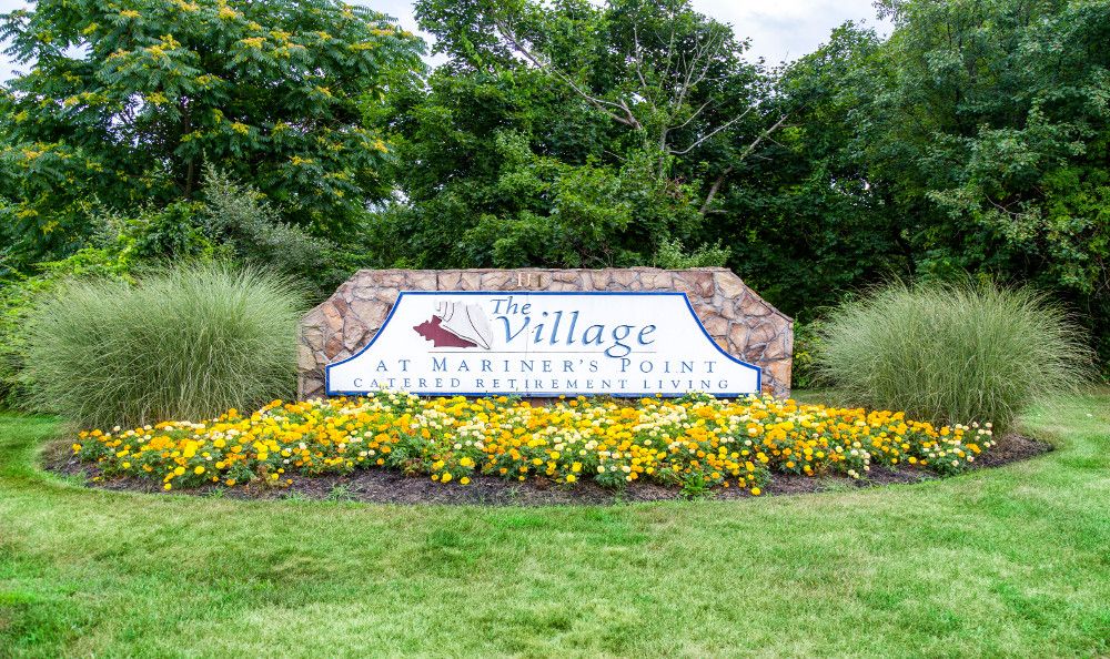 Entrance sign for the Village at Harbor Pointe, surrounded by flowers and greenery.