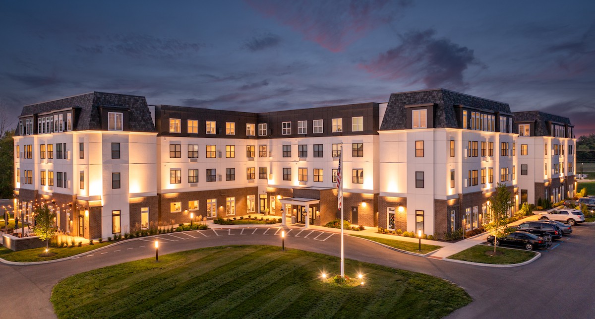 A well-lit hotel building at night with manicured lawns and a circular driveway.