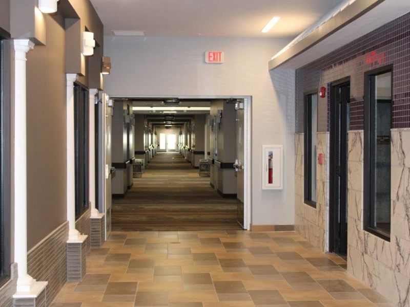 A well-lit indoor hallway with doors on both sides and a tiled floor.