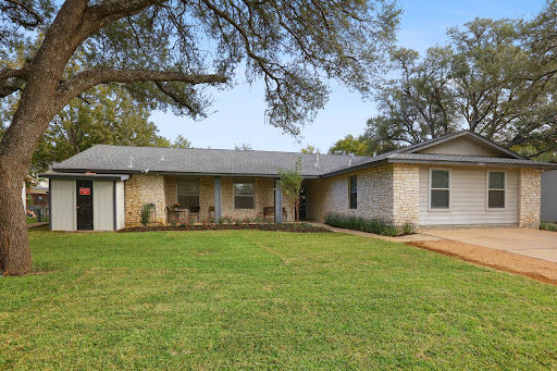 A charming single-story house with a spacious green lawn and shaded by trees.