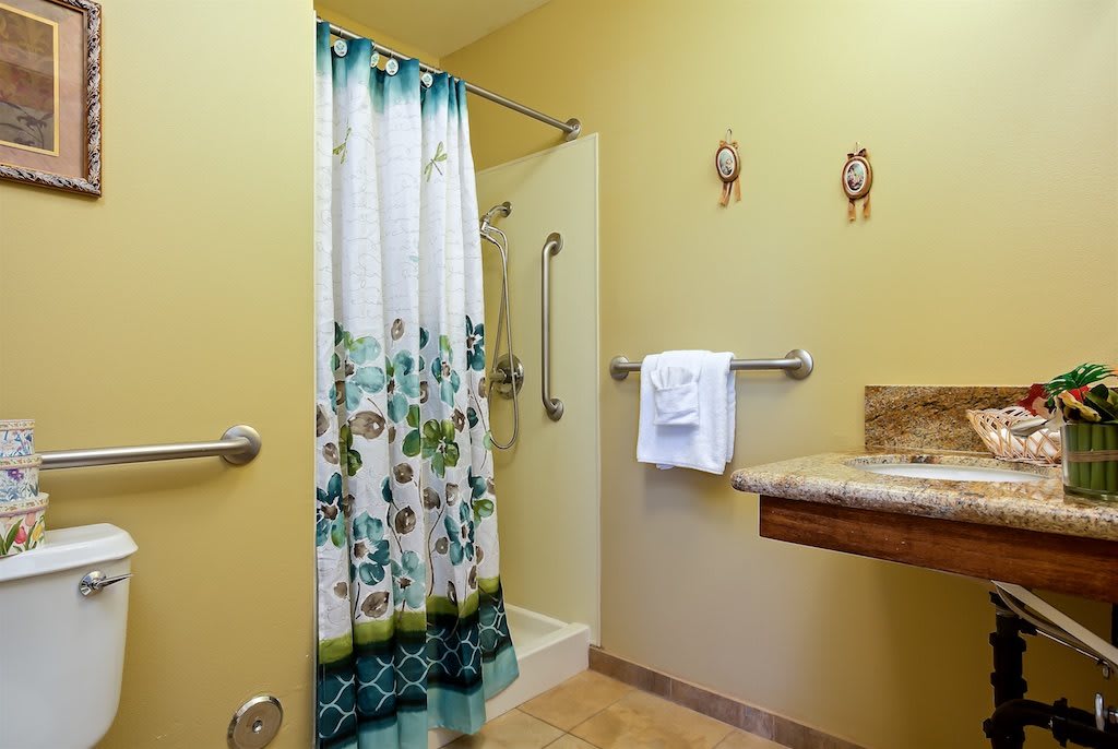 An accessible bathroom with a floral shower curtain, handrails, and yellow walls.