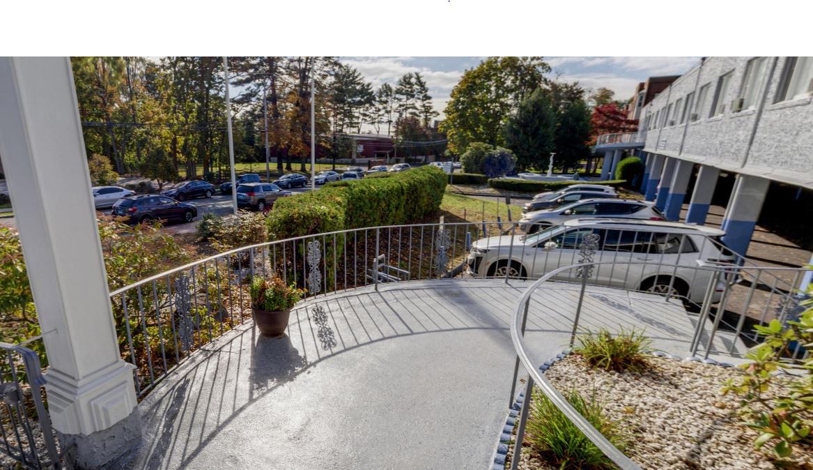 A view of a parking lot with several cars, surrounded by trees and a fenced pathway on a clear day.