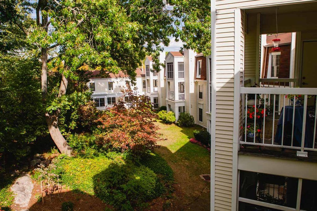 A view from a balcony overlooking a sunlit apartment courtyard with lush greenery.