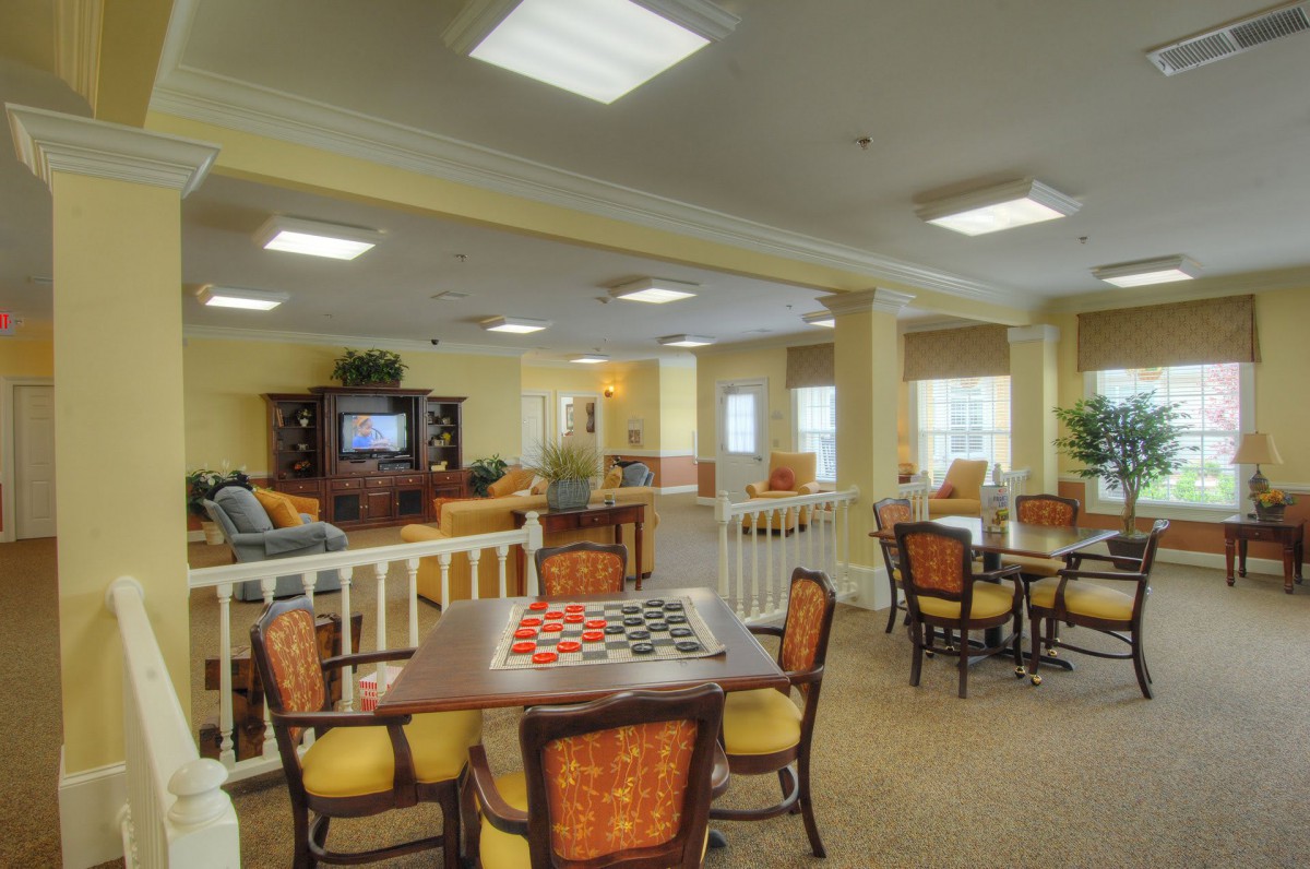 A cozy dining and recreational area with multiple tables, chairs, and a seating space illuminated by large windows.