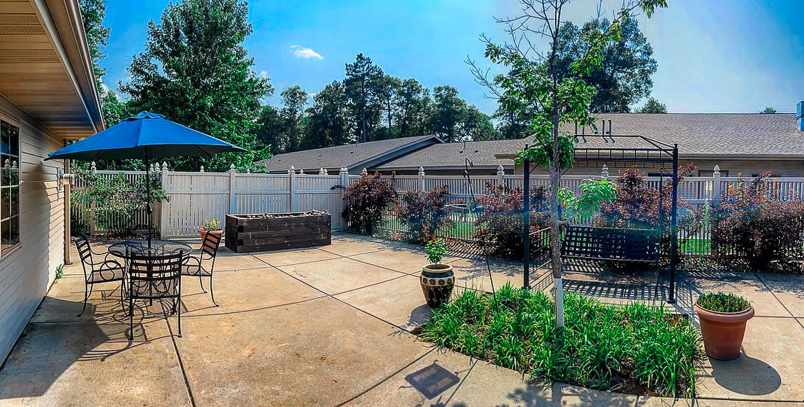 A sunny patio with plants, outdoor furniture, and a surrounding fence.
