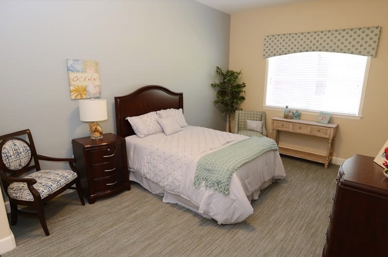 A cozy bedroom with a neatly made bed, nightstand, and window providing natural light.
