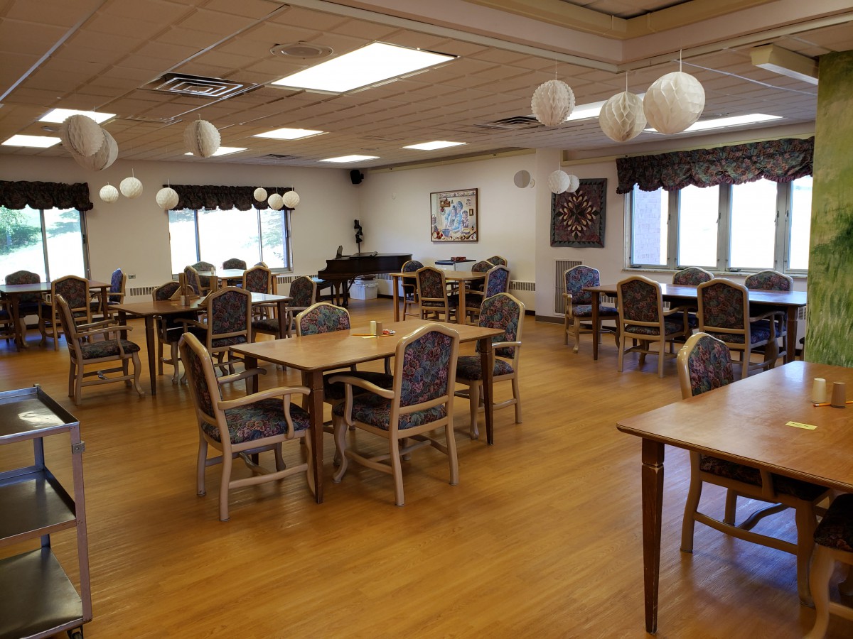 An empty dining room with wooden floors, tables, and chairs, decorated with hanging lights.