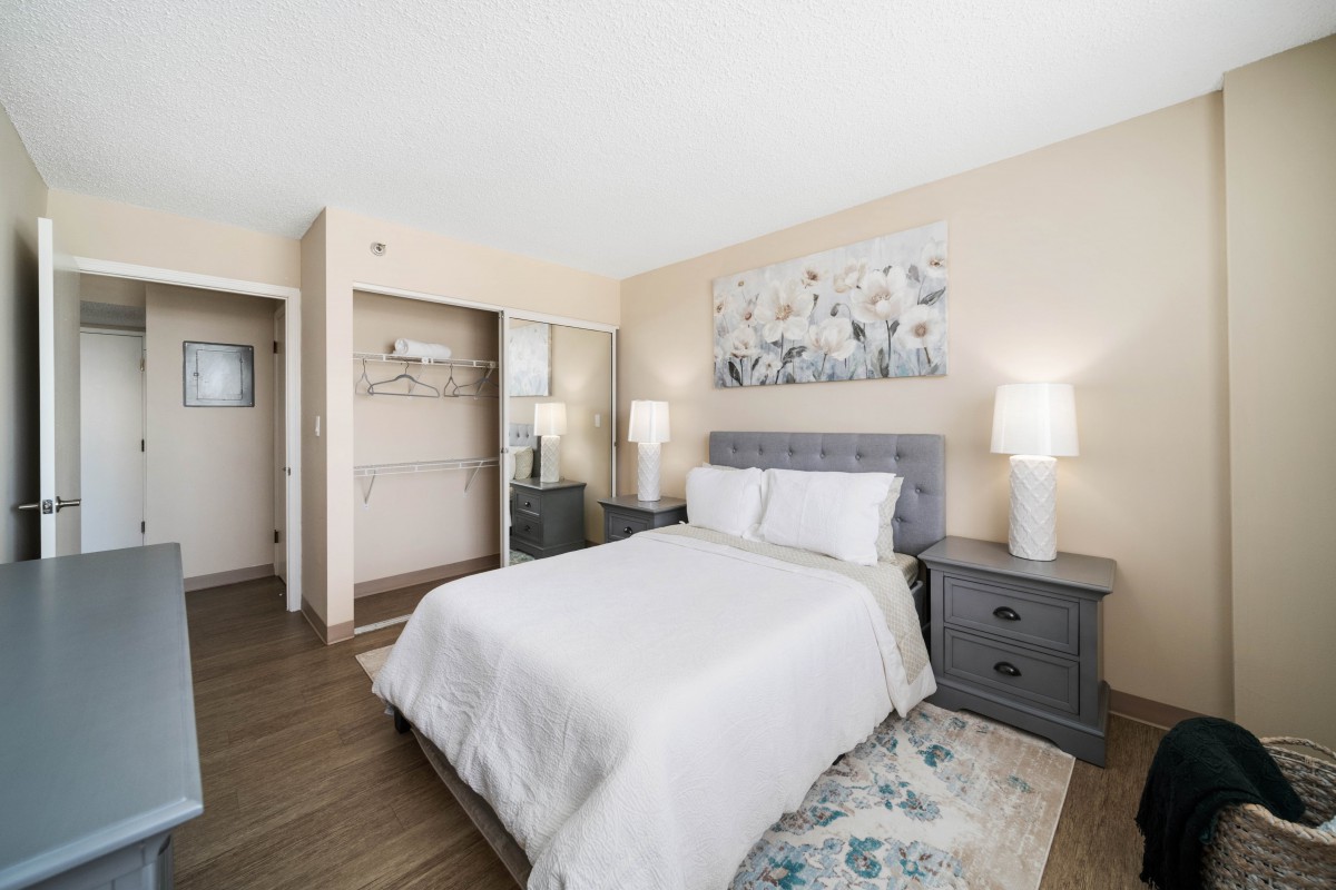 A neatly arranged bedroom featuring a bed with white bedding, two nightstands with lamps, and decorative artwork above the headboard.