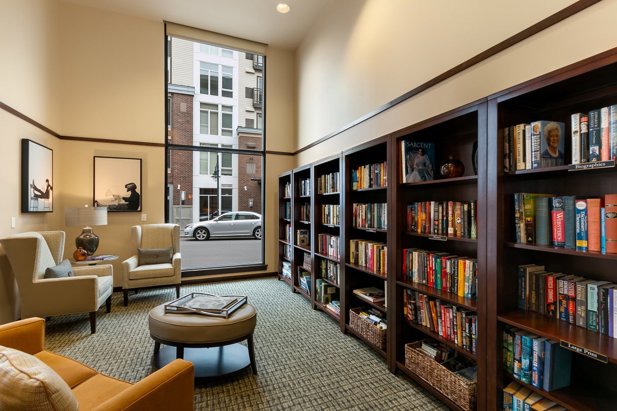 A cozy library reading area with bookshelves, comfortable chairs, and a large window.