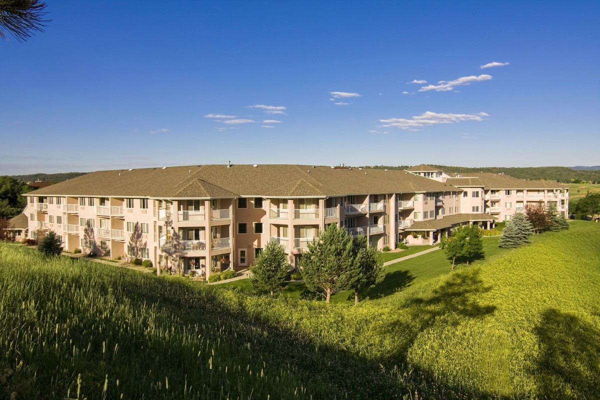 A peaceful apartment complex surrounded by lush greenery under a clear blue sky.