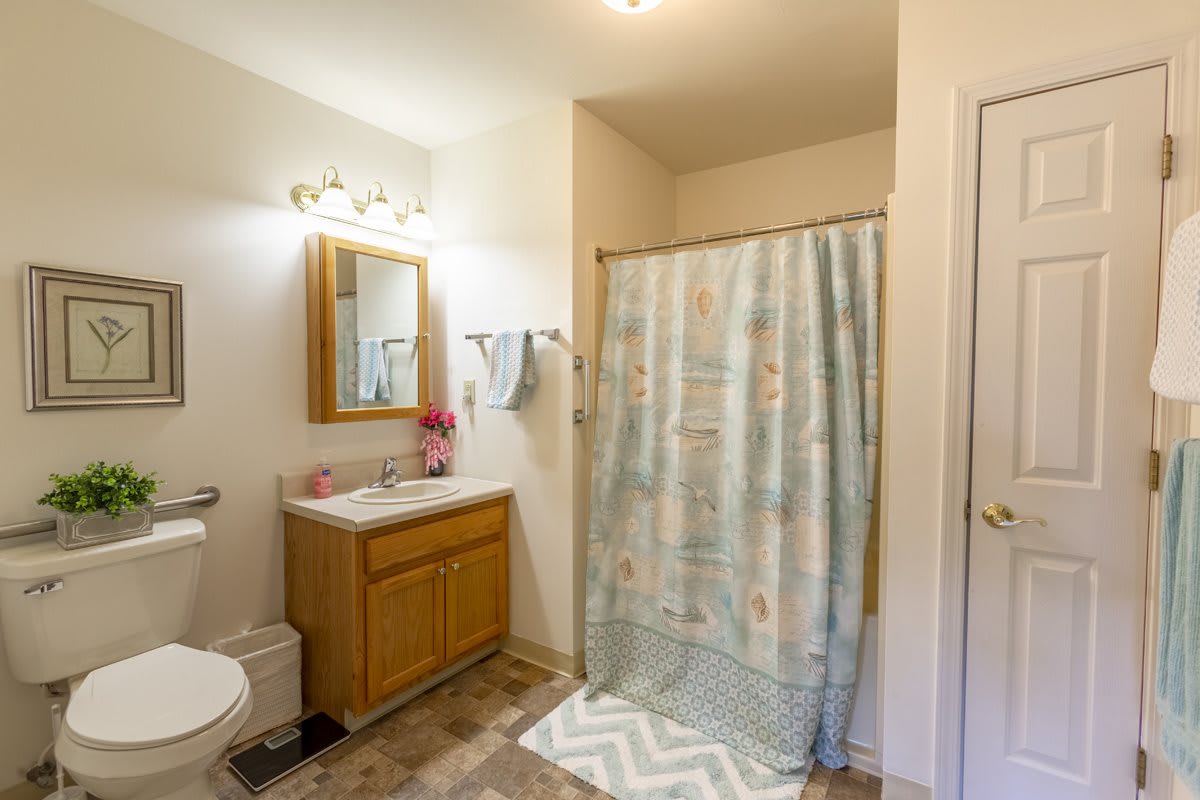 A well-lit bathroom featuring a vanity with mirror, shower curtain, and towels neatly arranged.