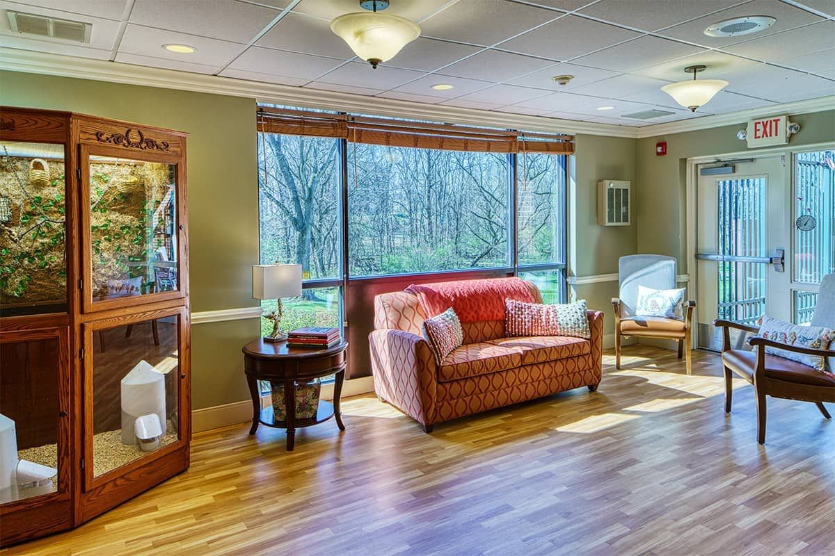 A cozy living room with a warm, inviting atmosphere featuring a couch, large windows, and wooden flooring.