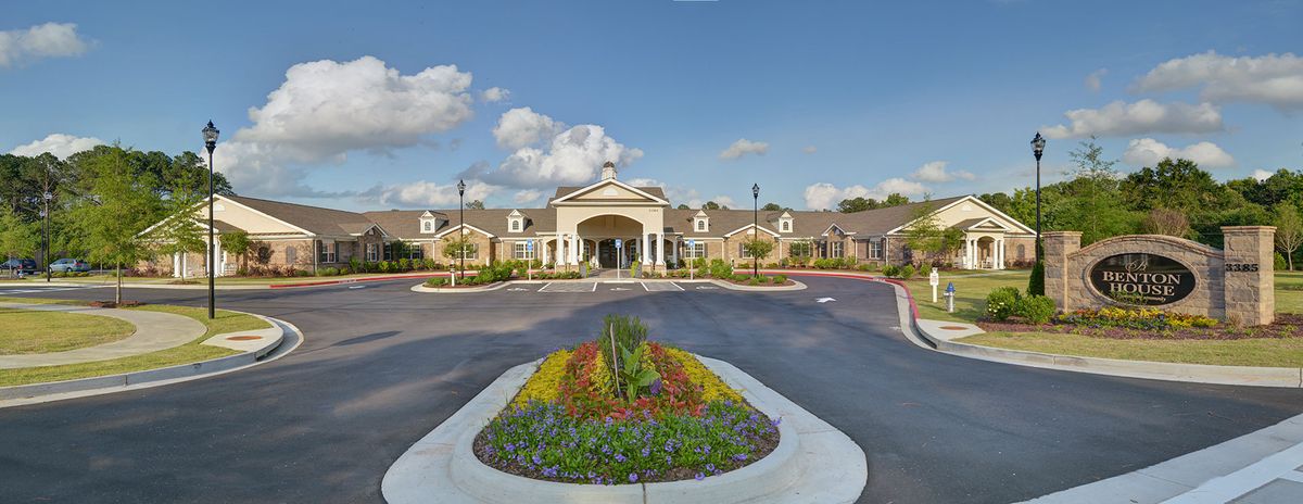 A grand entrance to a building with well-maintained landscaping under a partly cloudy sky.