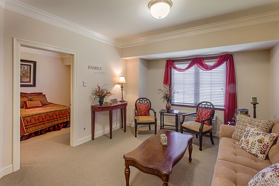 A cozy living room with traditional decor, featuring comfortable chairs, a wooden table, and elegant curtains.