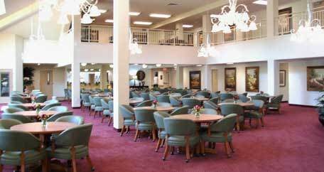 An elegant dining hall with neatly arranged tables and chairs, featuring soft lighting and a plush carpet.