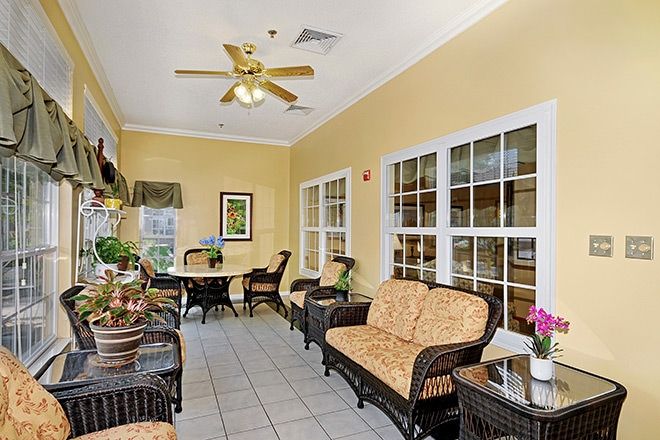 A cozy sunroom with wicker furniture, large windows, and a ceiling fan.