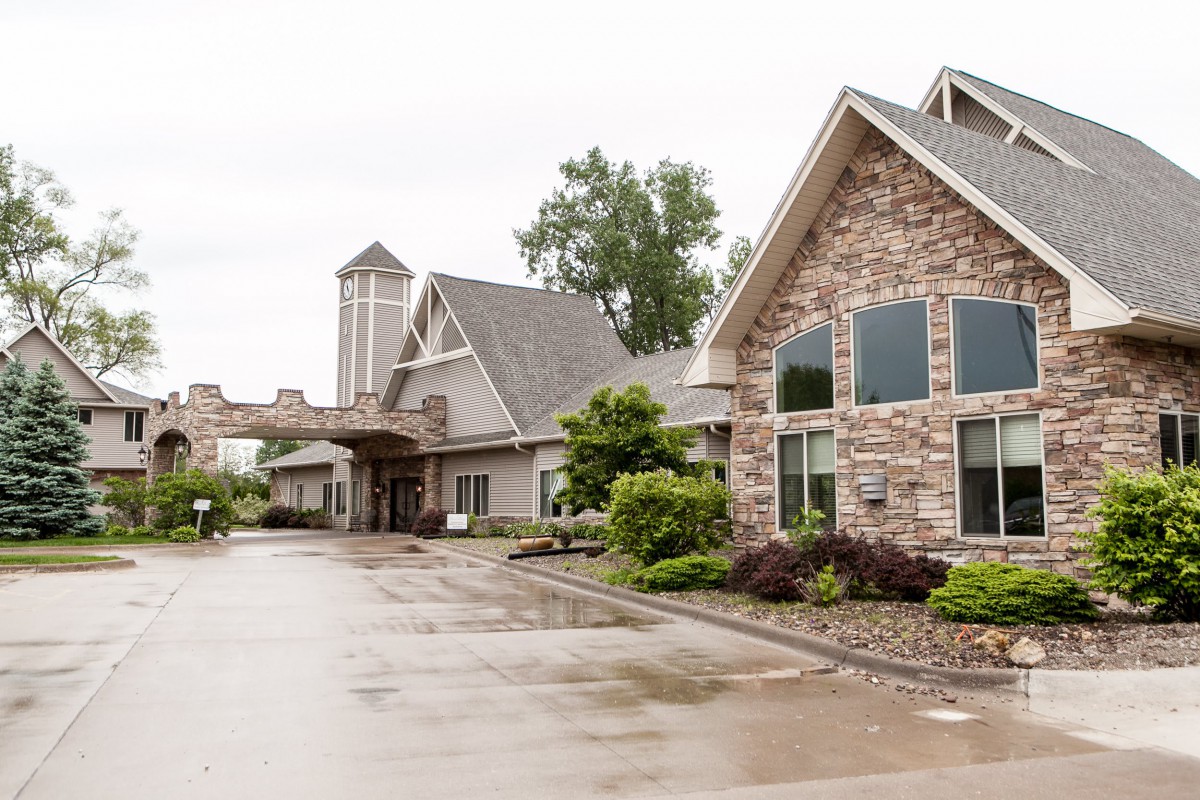 A stone-faced building with a driveway and surrounding greenery on an overcast day.