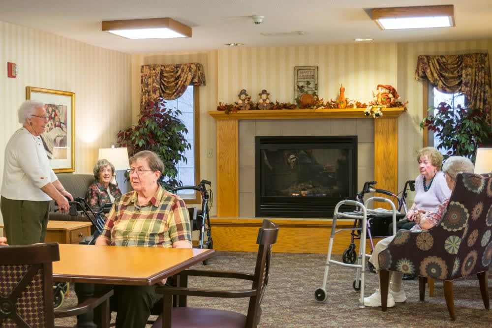 A community room in a nursing home with elderly residents sitting near a fireplace.