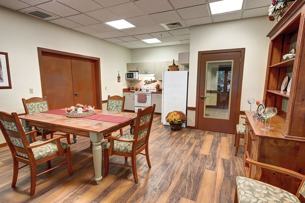 A cozy kitchen and dining area with a wooden table and chairs, featuring a refrigerator and a warm wooden floor.
