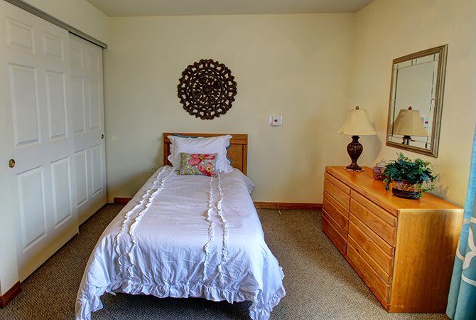 A cozy bedroom with a single bed, decorative wall art, and a wooden dresser topped with a lamp.