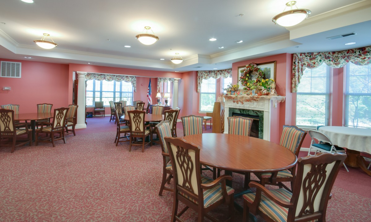 A warmly decorated dining room with multiple tables and chairs, featuring a fireplace and elegant lighting.