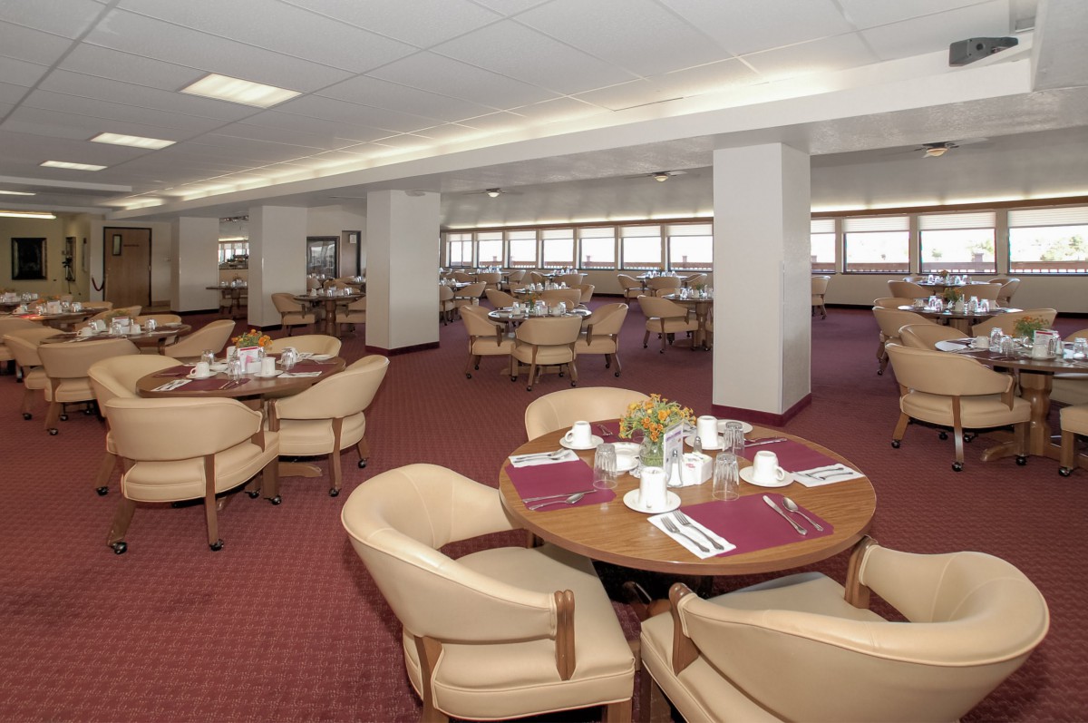 An indoor dining area with neatly arranged tables and chairs, featuring a carpeted floor and place settings.