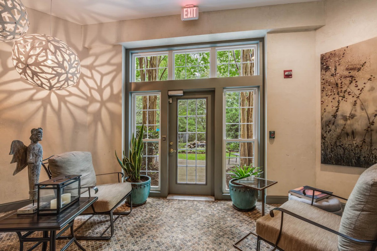A cozy lobby area with glass doors leading outside, featuring comfortable seating and decorative plants.