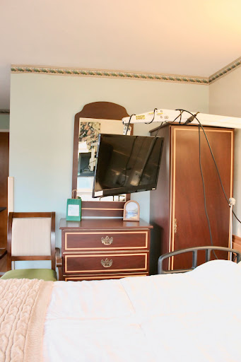 A cozy bedroom setup featuring a wall-mounted television, a mirror, and wooden furniture.