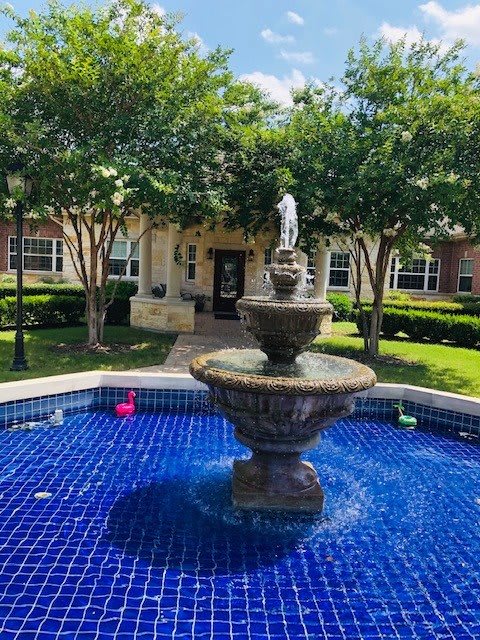 A picturesque fountain in a landscaped garden setting outside a building.
