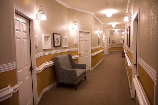 A warmly lit hallway with a carpeted floor, featuring framed artwork and a comfortable chair.