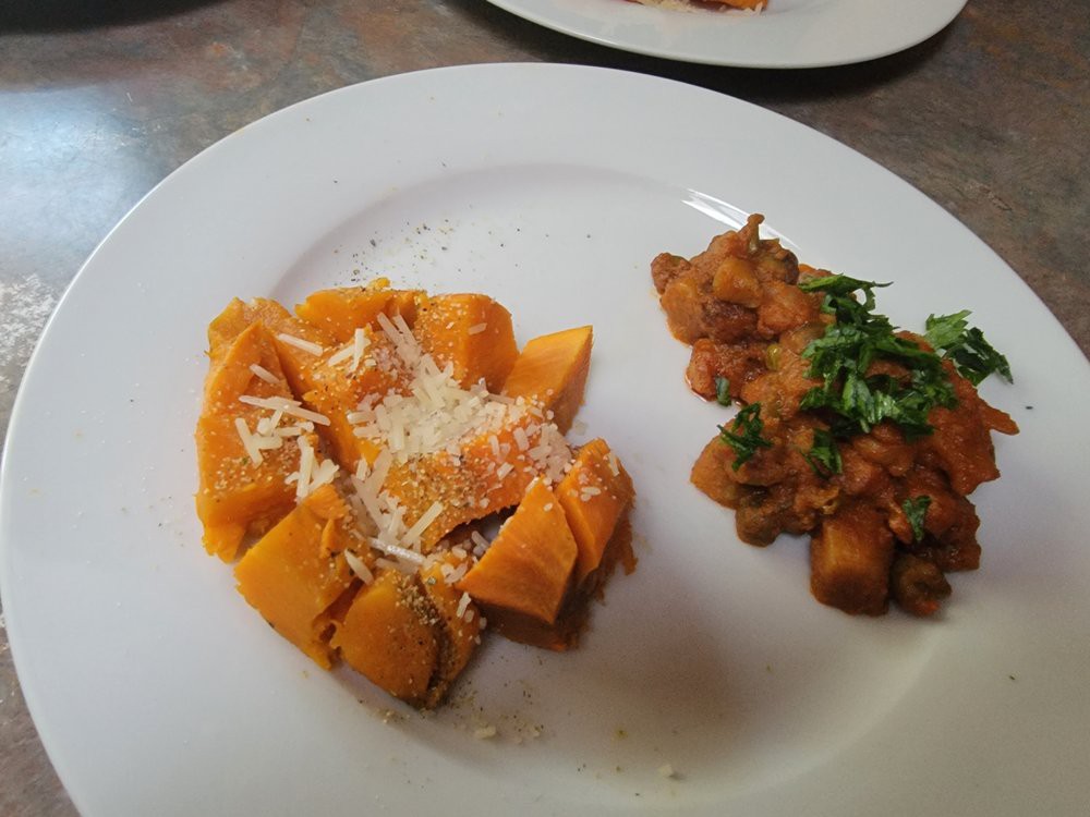 A plate featuring pumpkin gnocchi topped with Parmesan cheese and a side of savory stew garnished with fresh herbs.