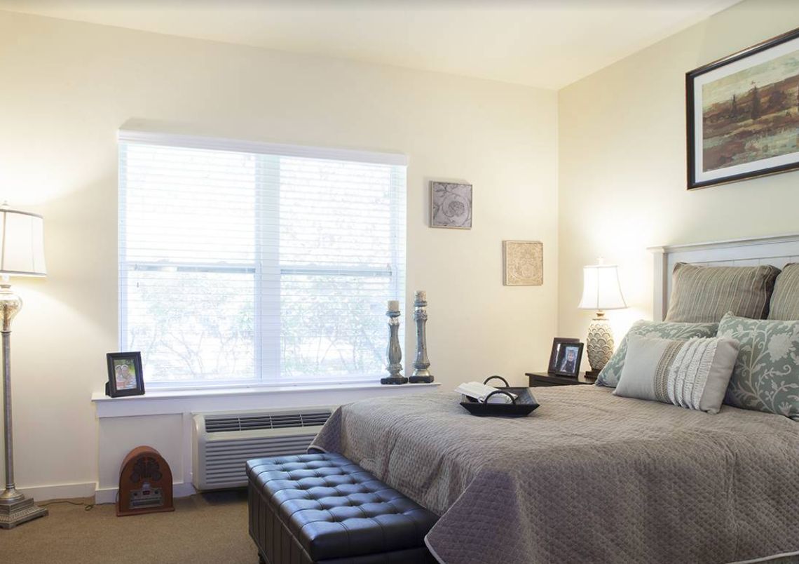A cozy bedroom with ample natural light coming through a large window, featuring a neatly made bed and stylish decor.