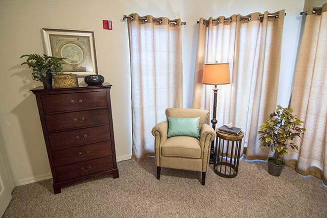 Cozy living room corner with an armchair, lamp, and chest of drawers.