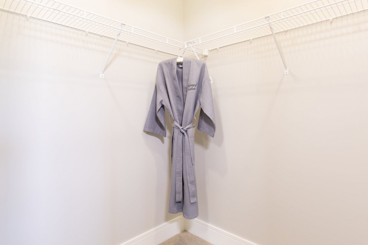 A gray robe hanging on a hanger in an empty closet.