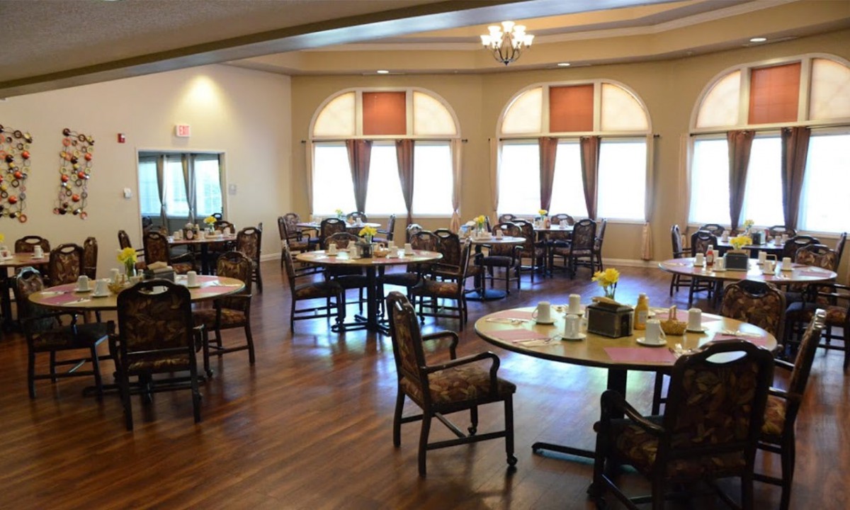 A spacious dining area with neatly arranged tables and chairs on a wooden floor, well-lit by natural light from the windows.