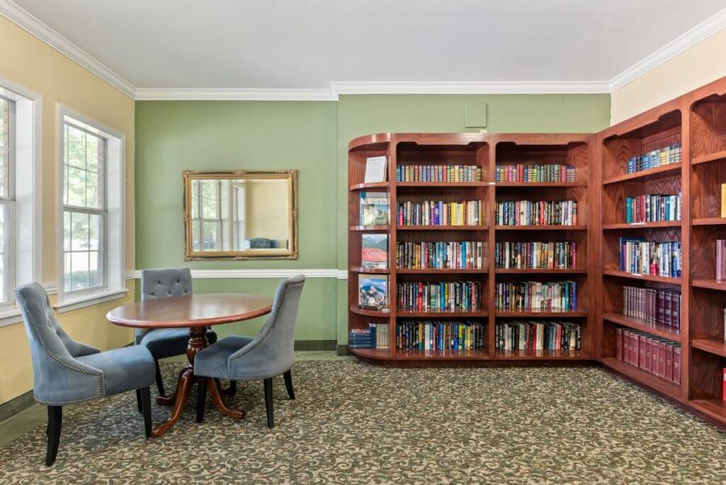 A cozy reading area featuring a bookshelf filled with books, a table with chairs, and a mirror on the wall.