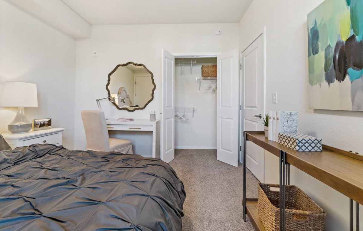 A cozy bedroom with a bed, desk, and mirror, featuring a small open closet.