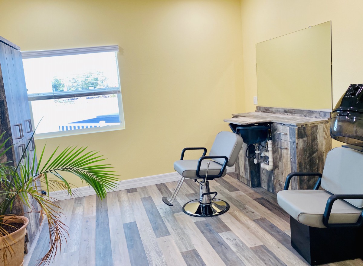 A modern hair salon with yellow walls, featuring styling chairs and a wash station.