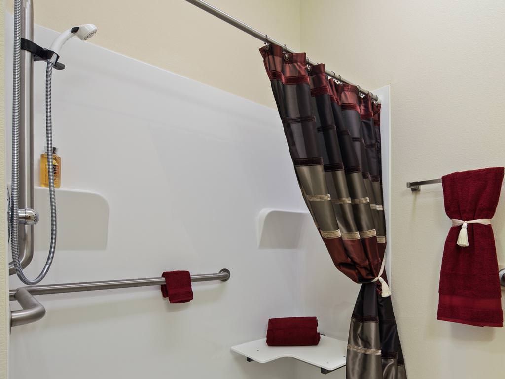 A bathroom with a colorful shower curtain, red towels, and a grab bar for safety.