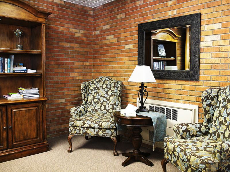 A cozy living room with brick walls, featuring floral armchairs, a small table, and a large mirror.