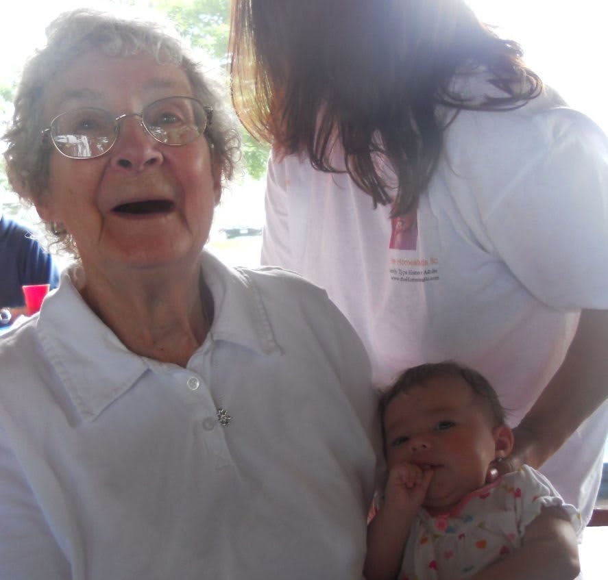 An elderly woman joyfully holding a baby, with another person nearby, showcasing a moment of family togetherness.