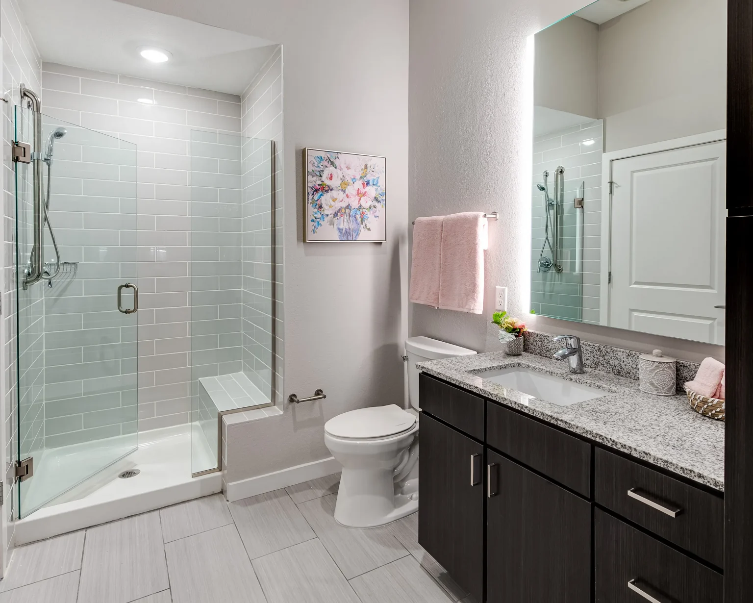 A modern bathroom with a glass-enclosed shower, a large mirror above a dark wood vanity, and soft lighting adds to the contemporary design.